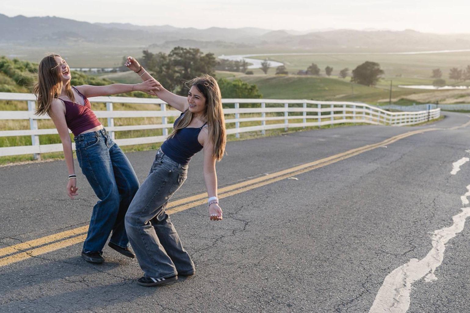 Two best friends laughing and dancing together on a country road at sunset