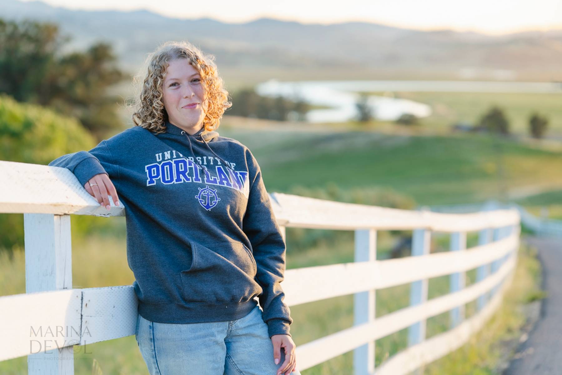 Senior leaning on a fence in a college hoodie