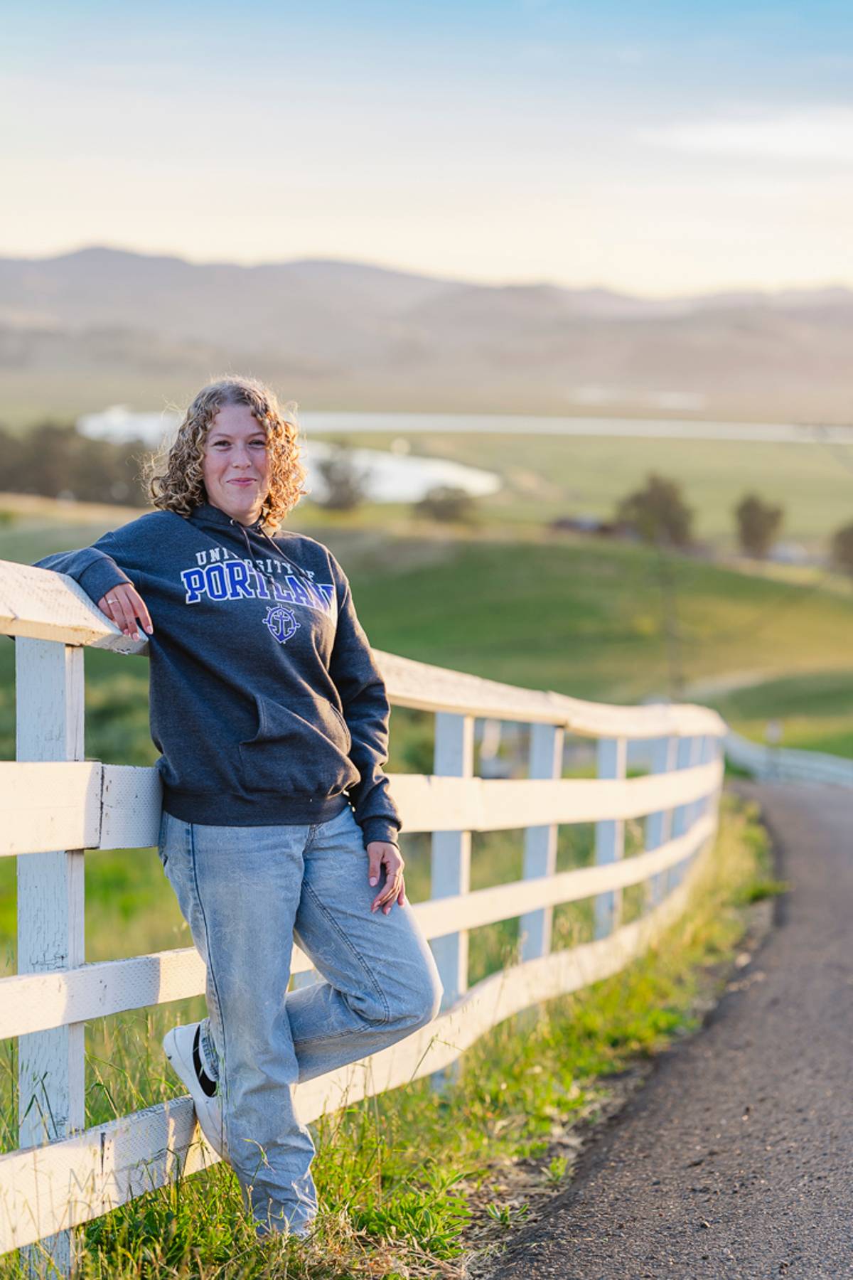 Senior leaning on a fence with a valley view behind her