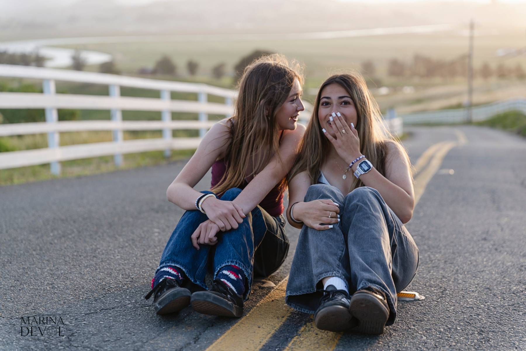 Two friends laughing while sitting on a country road