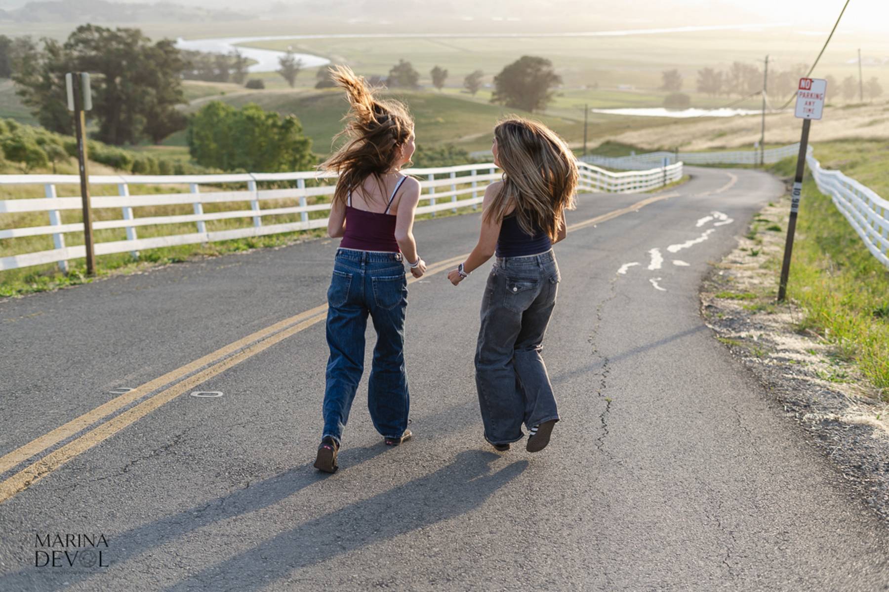Two friends walking away down a country road, hair in the wind