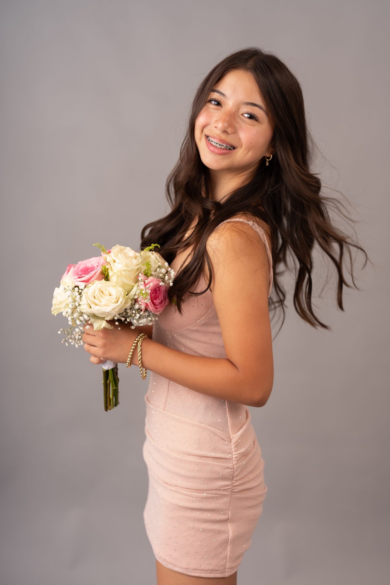 Senior in a blush dress smiling over her shoulder, holding a rose bouquet, studio portrait