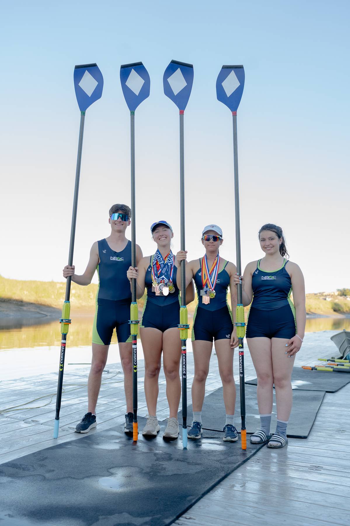 Rowing team posing with oars and medals at sunset